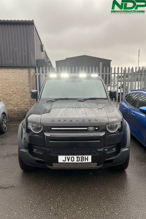 Land Rover Defender parked between two other cars with a visible brand logo in the background.